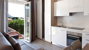 Una cocina moderna con armarios blancos, horno empotrado y un amplio ventanal con vistas a zonas verdes y edificios.