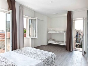 Une chambre avec un lit superposé, un lit simple et un balcon avec des rideaux.
