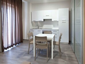 Une cuisine moderne avec des meubles blancs, une table à manger avec des chaises et une fenêtre avec des rideaux.