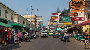 A bustling street with various shops and signs, including a Buddy Beer sign and a True restaurant. - The House Hostel (Bangkok)