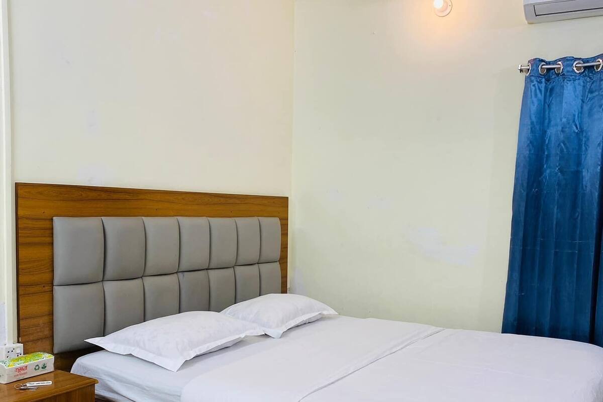 A neatly made bed with white linens, a wooden headboard, and a nightstand with a lamp and a box of tissues.