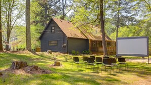 A rustic cabin with a large screen and chairs arranged for an outdoor event. - Deck & Hiking Trails: Luxe Georgia Farm Retreat (Lithonia)