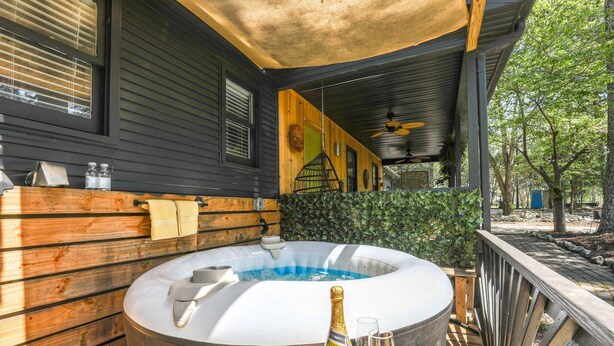 A hot tub with a wooden deck, a bottle of champagne, and two glasses on a table. - Deck & Hiking Trails: Luxe Georgia Farm Retreat (Lithonia)