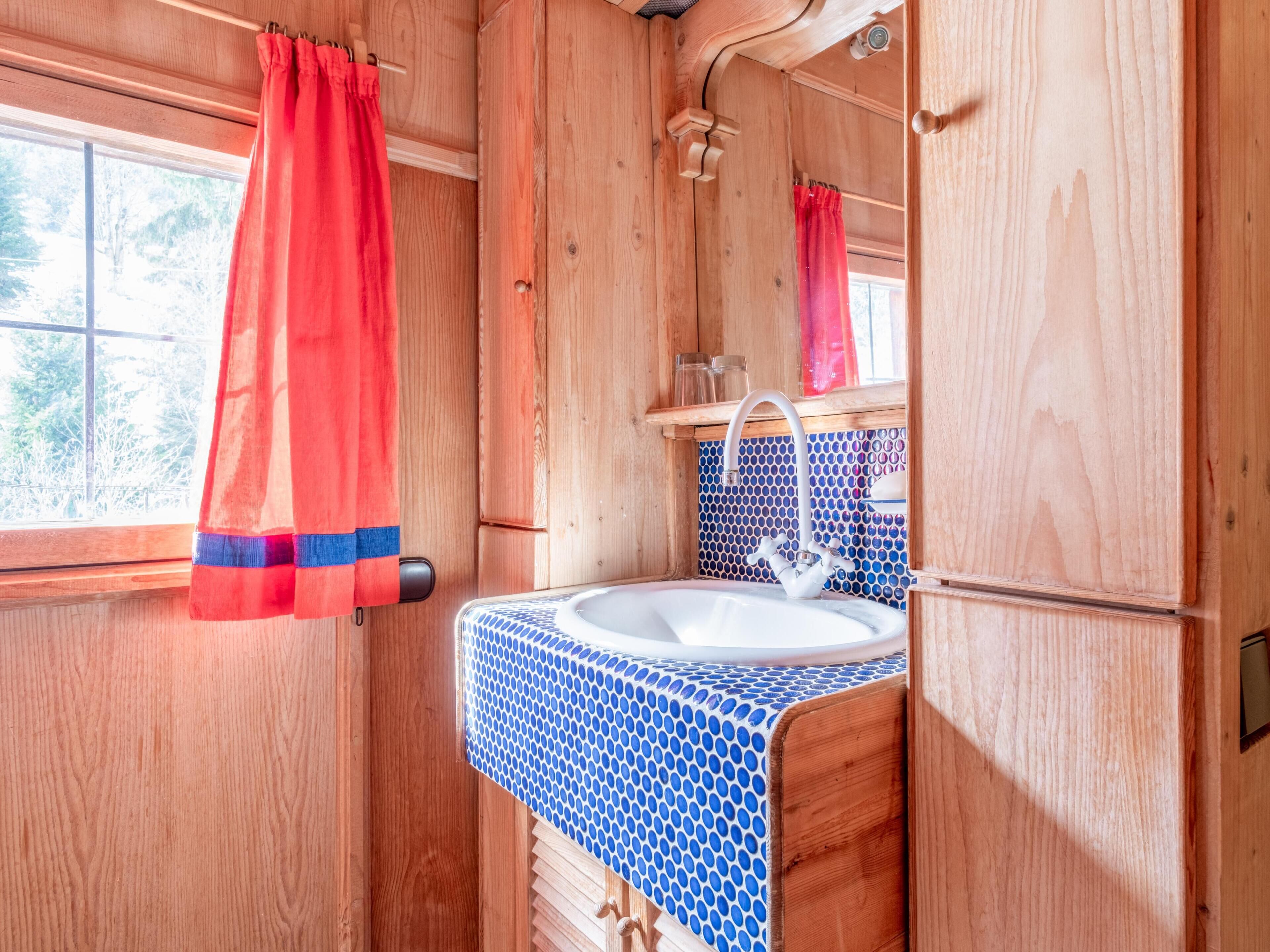 Ein Badezimmer einer Holzhütte mit Fenster, Waschbecken mit blau gemustertem Ablagetisch und rotem Duschvorhang.