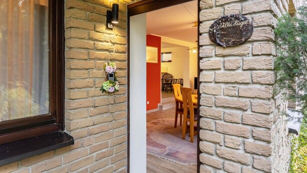 Pared exterior de ladrillo con una puerta que da a un comedor interior con sillas de madera y una mesa.
