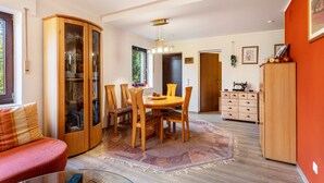 Un comedor con una mesa redonda y sillas, un mueble de madera con puertas de cristal y una pared roja con un cuadro enmarcado.