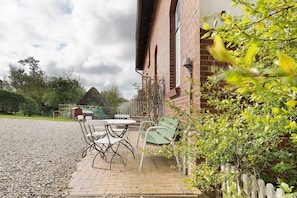 A patio area with outdoor seating, a brick building, and a gravel path. - Apartment 'Hof Voege Ferienwohnung 3' with Shared Garden and Wi-Fi (Brodersdorf)