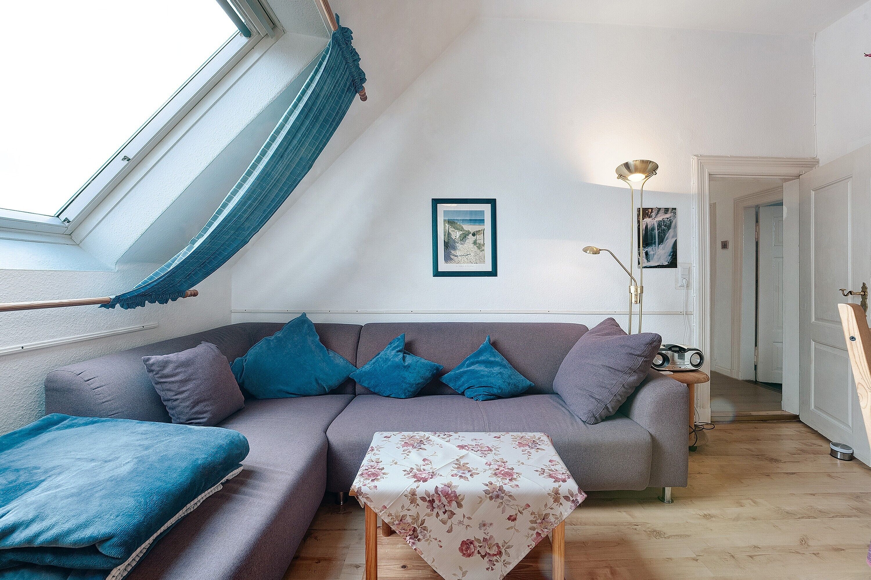 A room with a sofa, a small table, a framed picture on the wall, a lamp, and a door leading to another room.
