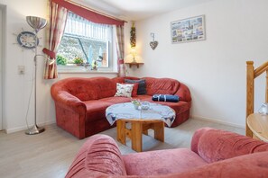 A cozy living room with a red sofa, a wooden coffee table, and a window with curtains.