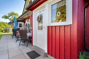 A red building with a white door, a window with a wreath, and outdoor seating with chairs and a table. - Holiday Apartment "Fewo 31 - Halbinsel Darss - Ostsee
" with Private Terrace, Shared Garden & Wi-Fi (Wieck am Darß)