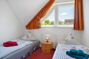 A bedroom with two beds, a nightstand, a lamp, and a window with curtains. - Holiday Apartment "Fewo 31 - Halbinsel Darss - Ostsee
" with Private Terrace, Shared Garden & Wi-Fi (Wieck am Darß)