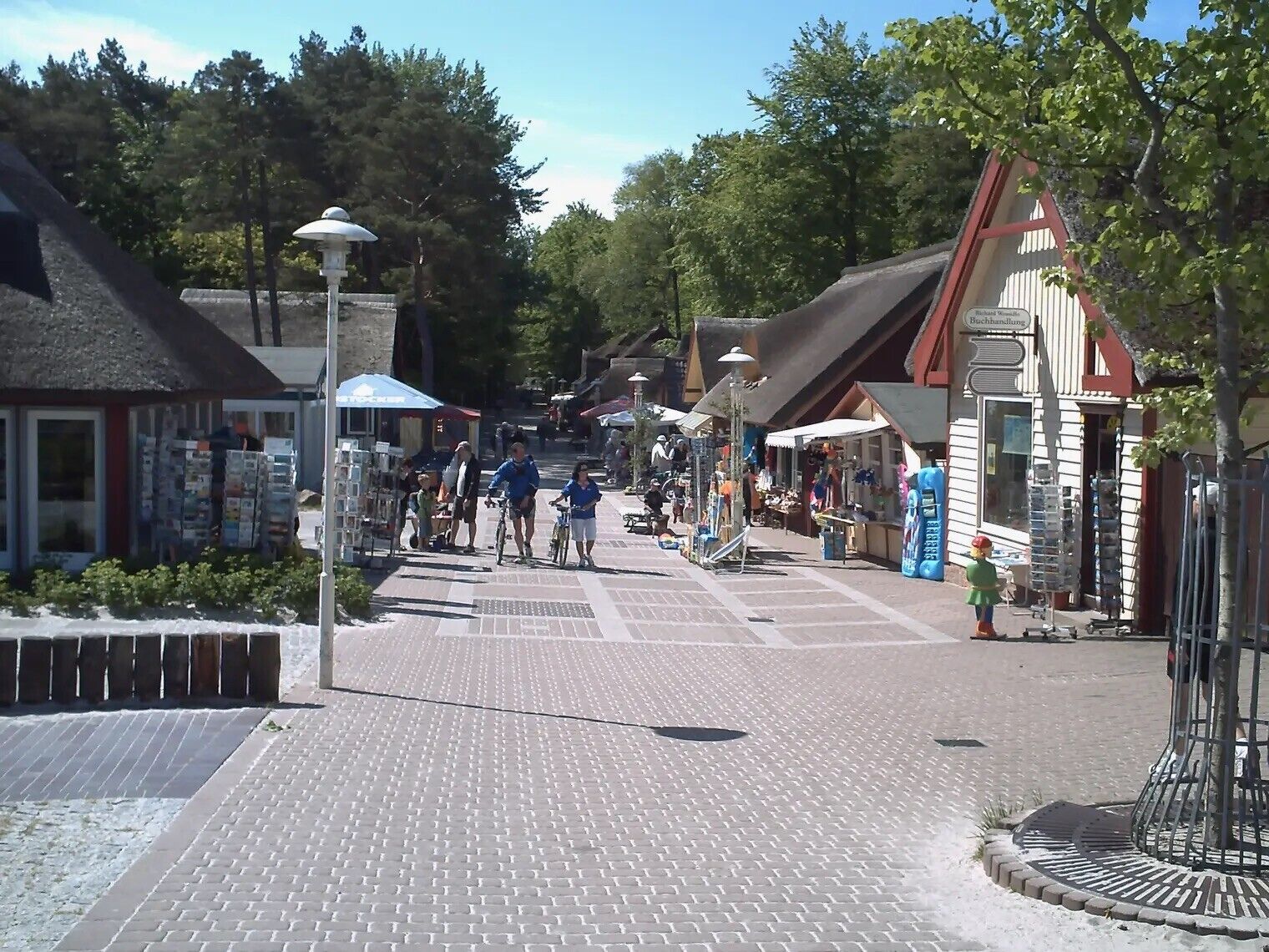 Une rue pavée bordée de boutiques et d’immeubles, une zone piétonne où l’on peut voir des gens se promener et faire du vélo, et un lampadaire.