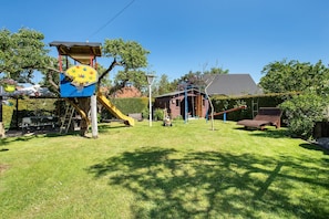 A backyard with a play structure, a slide, a swing set, and a small shed.