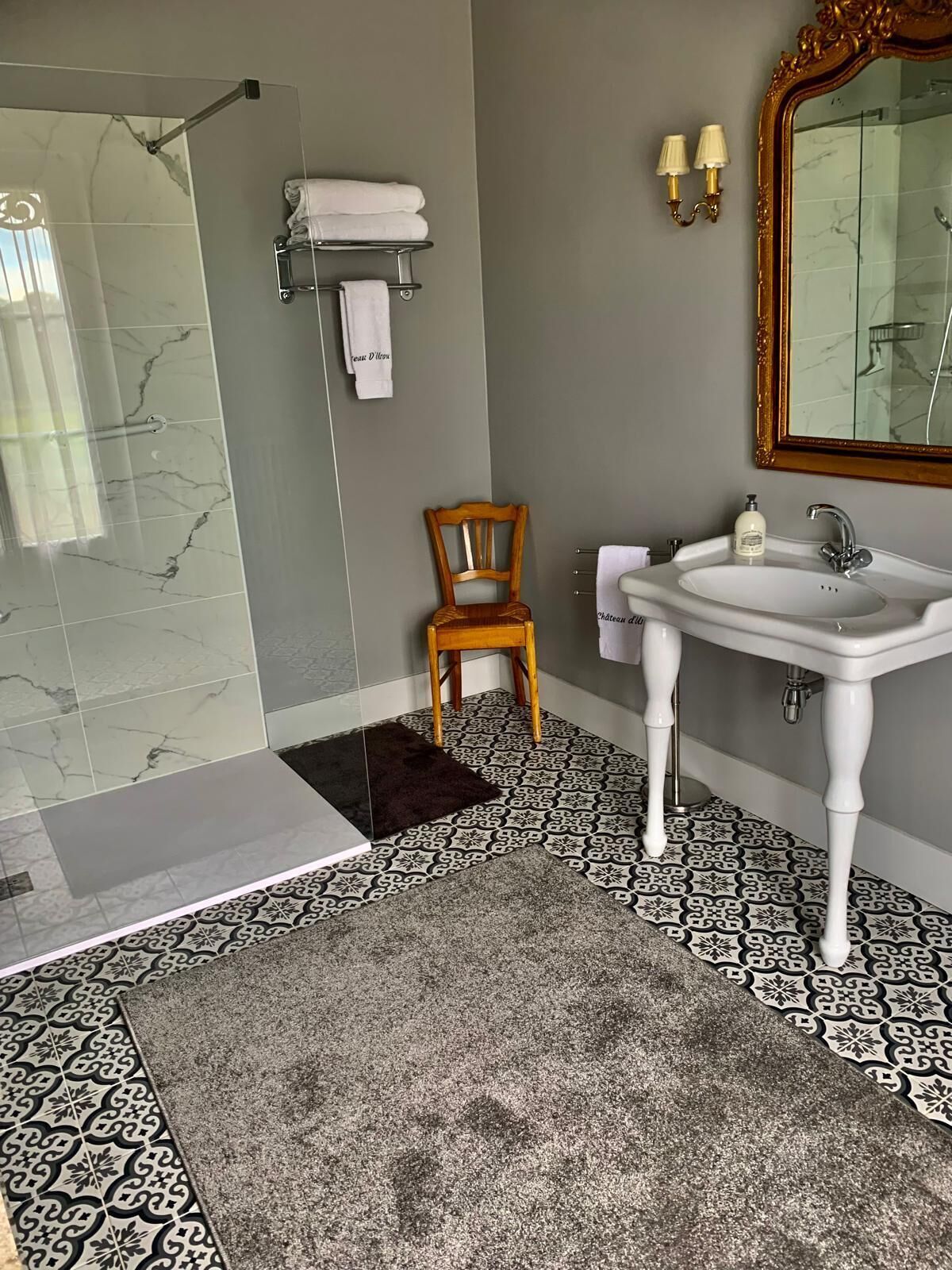 A bathroom with a shower, a sink, a chair, and a mirror.