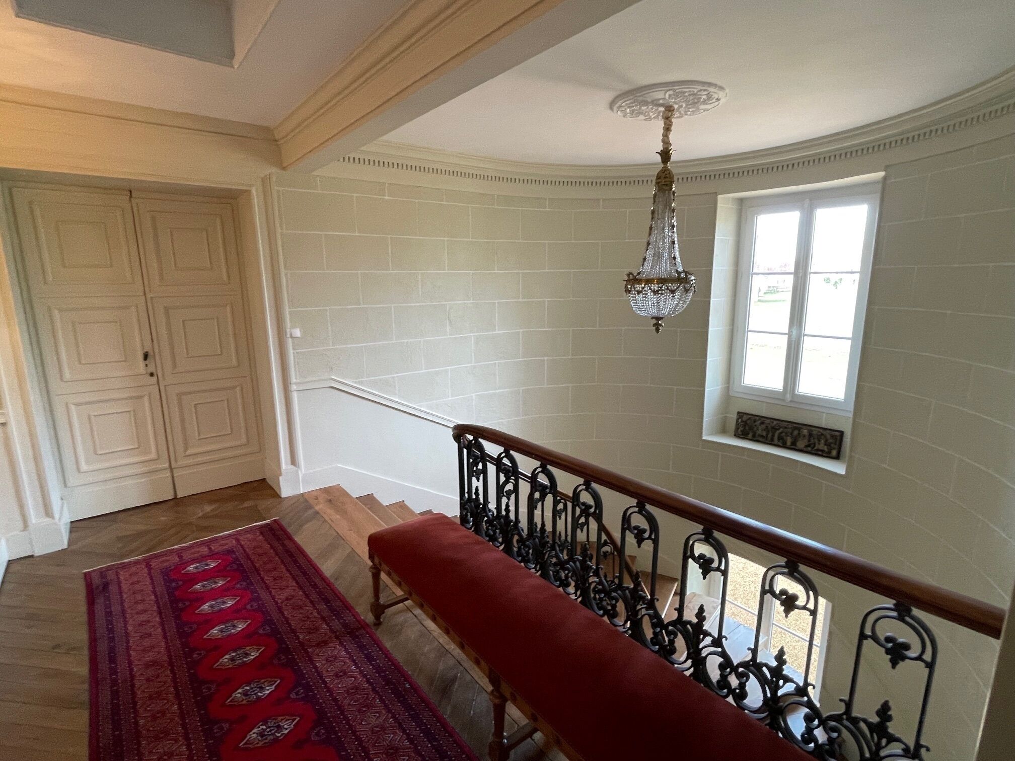 Eine Treppe mit einer roten Bank, weiß gefliesten Wänden und einem Chandelier.
