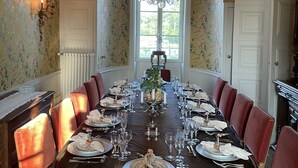 Une salle à manger élégante, avec une longue table dressée pour un repas, entourée de chaises à revêtement rouge.