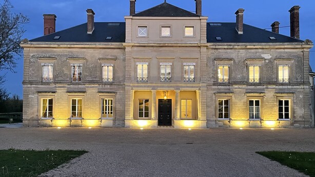 Un grand bâtiment en pierre à deux étages, doté d’une façade symétrique, de fenêtres régulièrement espacées et d’une entrée centrale avec une porte noire.