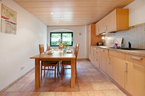 A modern kitchen with wooden cabinets, a dining table with chairs, and a window with a view of greenery.