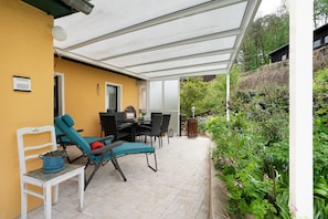 A covered patio with outdoor furniture, a table, and a potted plant.