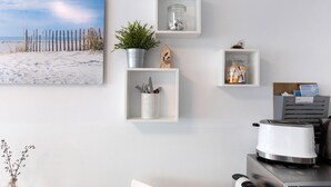 Ein Zimmer mit einem Strandgemälde, weißen Regalen mit diversen Gegenständen und einem Toaster auf der Arbeitsfläche.