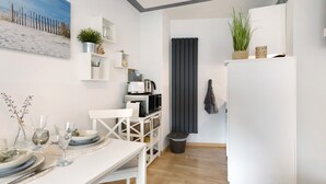 Eine moderne Küche mit weißen Schränken, einem Esstisch für zwei Personen, einer Kaffeemaschine und einem kleinen Blumentopf auf der Arbeitsfläche.