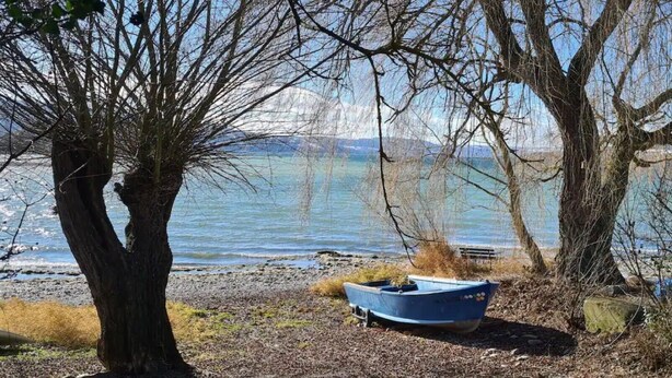 Ein Boot an einer felsigen Küste, im Hintergrund Bäume und ein Gewässer.