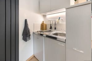 A compact kitchen with a sink, a wooden cutting board, and kitchen utensils hanging on the wall. - Apartment 'Am Hohentwiel' with Mountain View, Private Terrace and Wi-Fi (Singen (Hohentwiel))