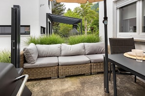A wicker sofa with cushions, a table with a glass, and a pergola in a garden setting. - Apartment 'Am Hohentwiel' with Mountain View, Private Terrace and Wi-Fi (Singen (Hohentwiel))