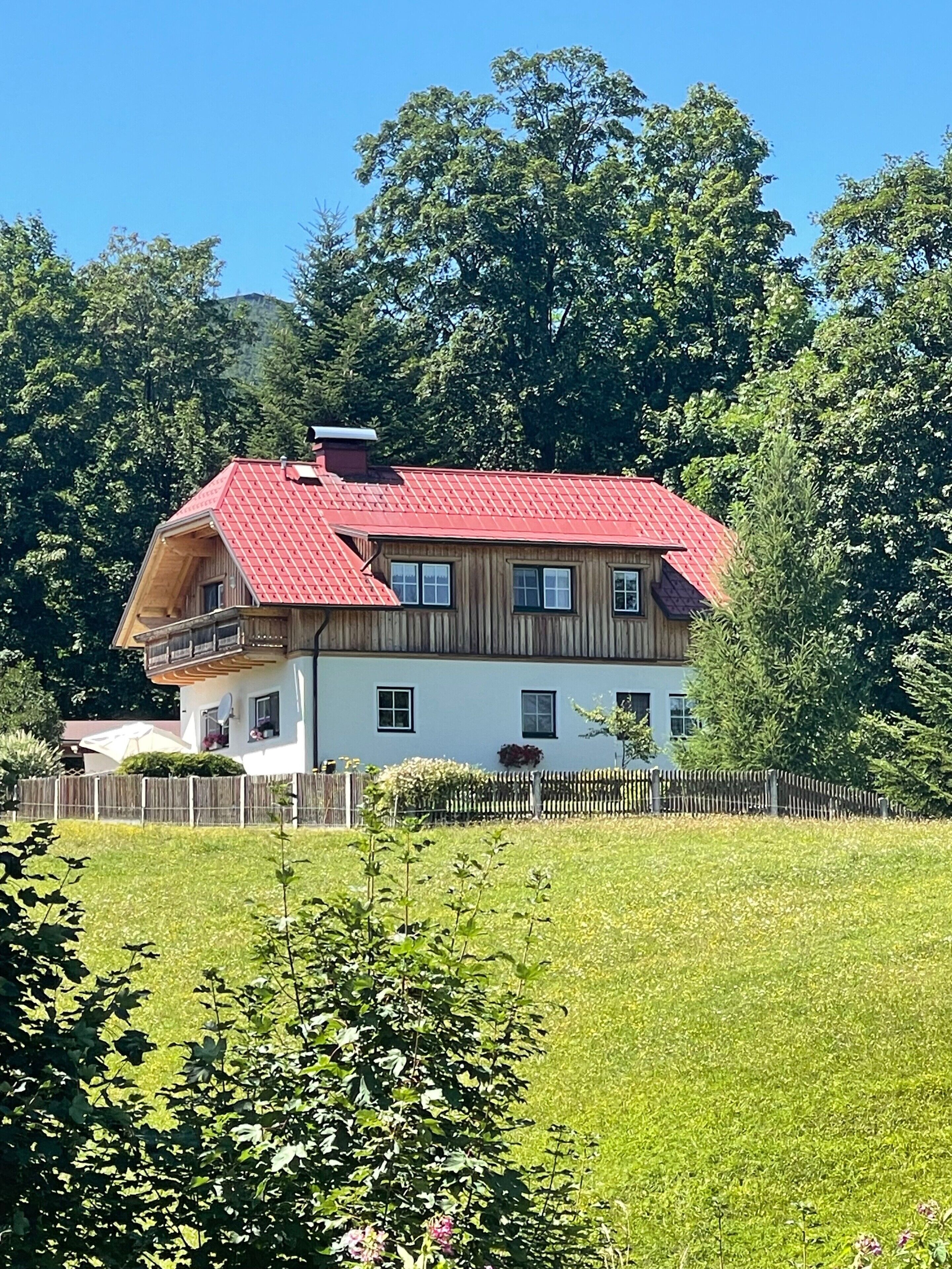 Ein zweistöckiges Haus mit rotem Dach, Holzfassade und einem Balkon.