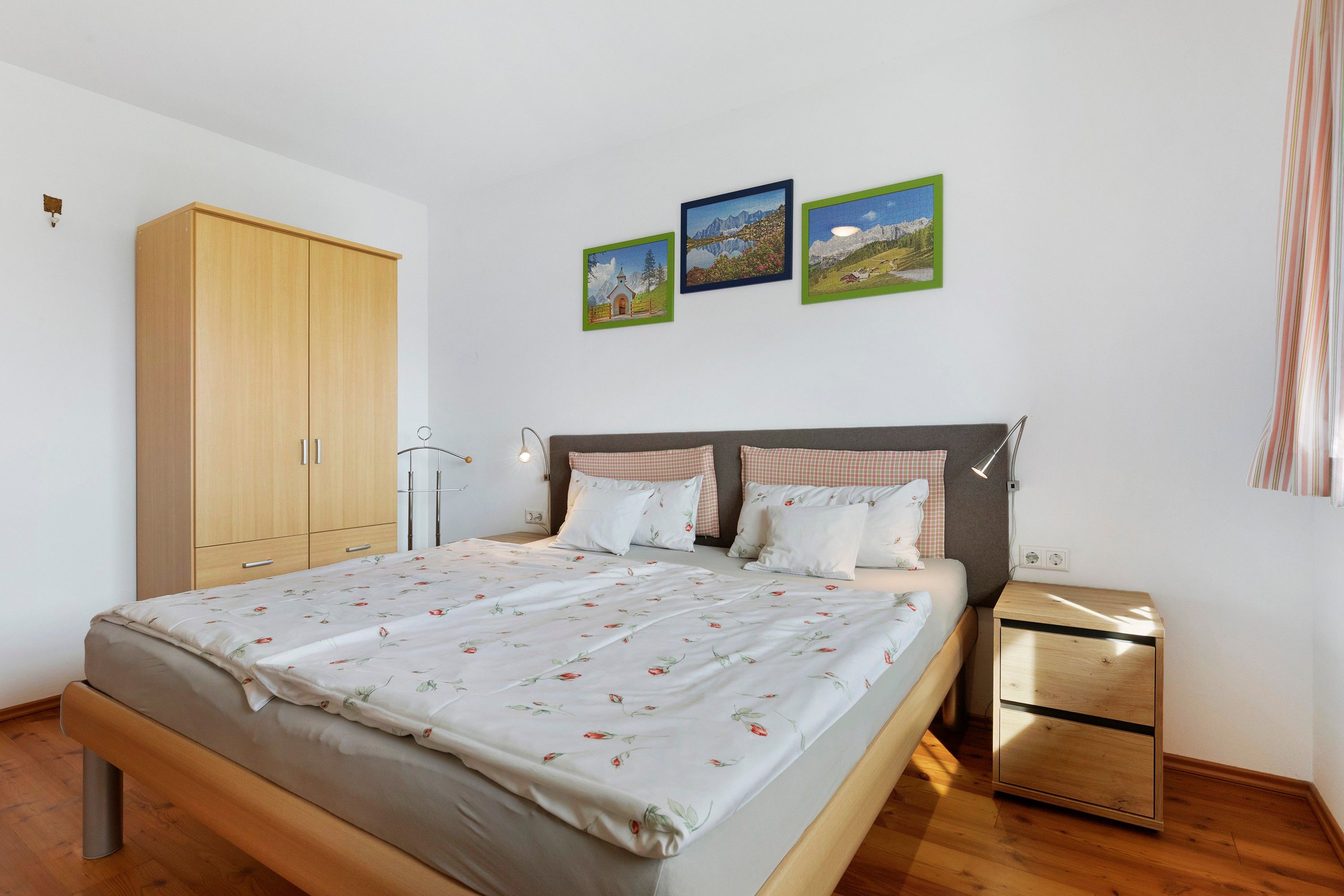 A bedroom with a bed, a wardrobe, a bedside table, and three framed pictures on the wall.