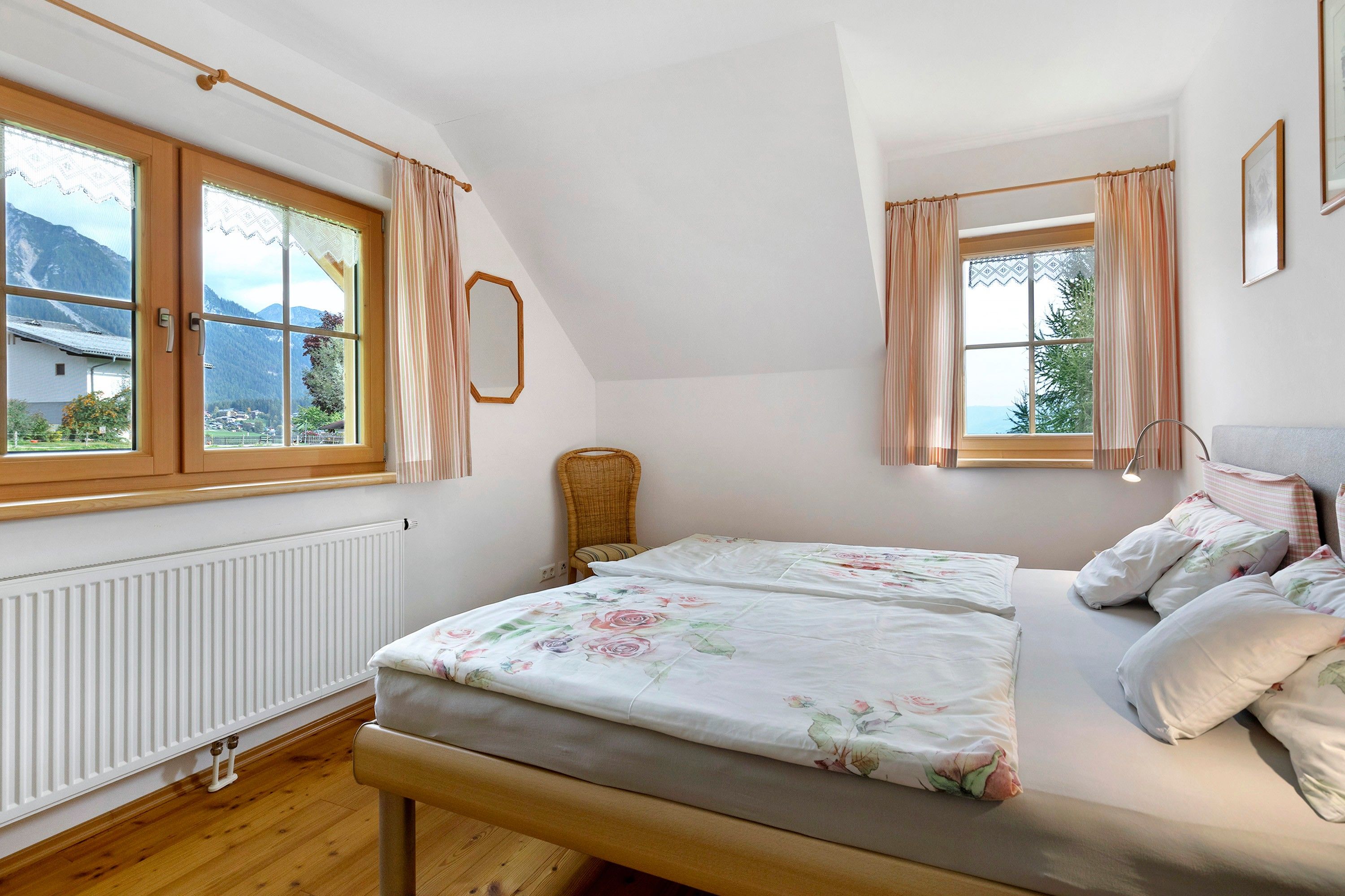 Ein Schlafzimmer mit zwei Betten, einem Fenster mit Vorhängen, einer Heizung und Blick auf Berge.