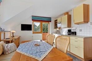 A compact kitchen with a dining area, featuring a table with a patterned tablecloth, wicker chairs, and wooden cabinets. - Apartment 'Haus Rosenheim' with Mountain View, Balcony and Wi-Fi (Ramsau am Dachstein)