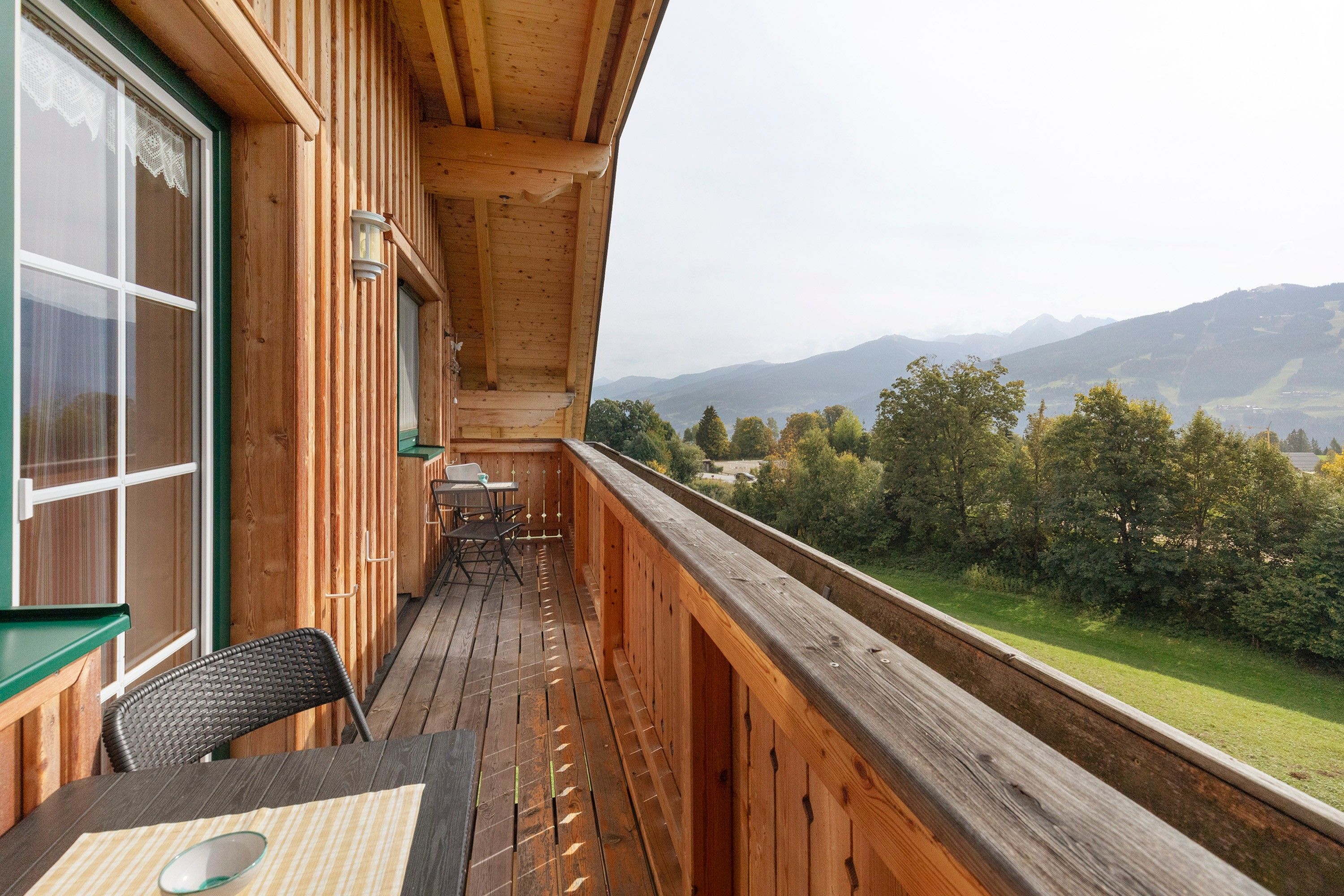 Un balcon en bois, agrémenté d’une table et de chaises, qui offre une vue sur un paysage montagneux.