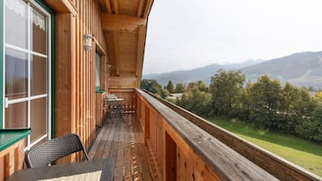 Un balcon en bois, agrémenté d’une table et de chaises, qui offre une vue sur un paysage montagneux.