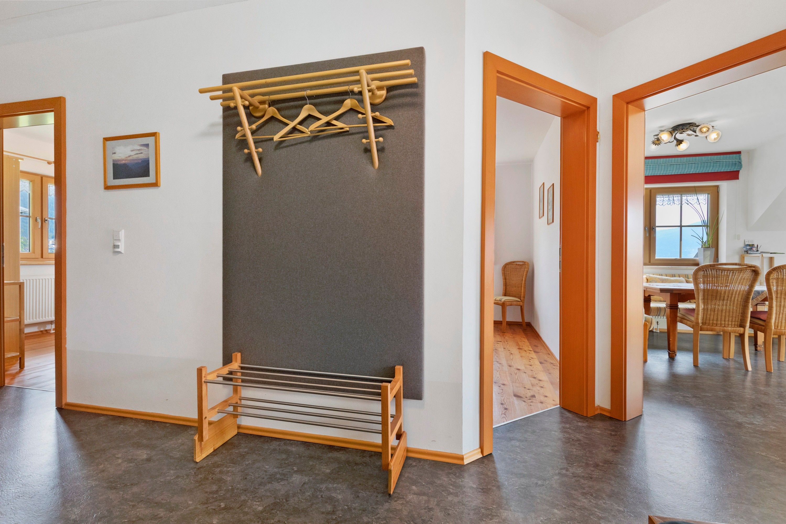 Ein Zimmer mit einem hölzernen Wäscheständer, einem gerahmten Bild an der Wand und Blick in einen angrenzenden Raum mit Essbereich.