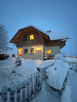 Ein Holzhaus mit verschneitem Dach und beleuchtetem Eingang.