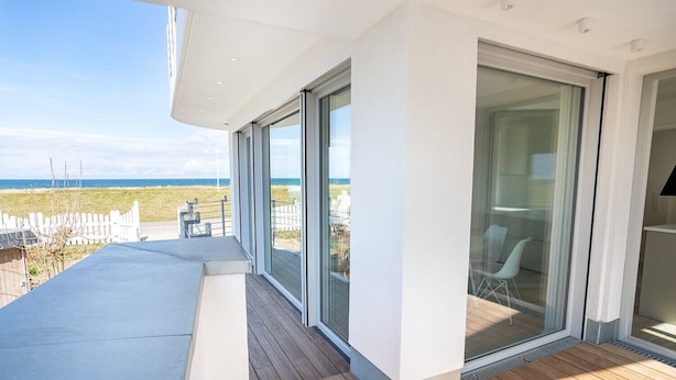 A modern building with large glass doors leading to a deck with a view of the beach. - Apartment 'Ferienwohnung Backbord' with Sea View, Shared Garden and Wi-Fi (Schönberg-Kalifornien)