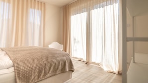 A bedroom with a bed, a chair, and large windows with sheer curtains. - Apartment 'Ferienwohnung Backbord' with Sea View, Shared Garden and Wi-Fi (Schönberg-Kalifornien)