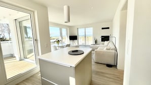 A modern kitchen with a central island, a dining area with a table and chairs, a sofa, and a TV mounted on the wall. - Apartment 'Ferienwohnung Backbord' with Sea View, Shared Garden and Wi-Fi (Schönberg-Kalifornien)