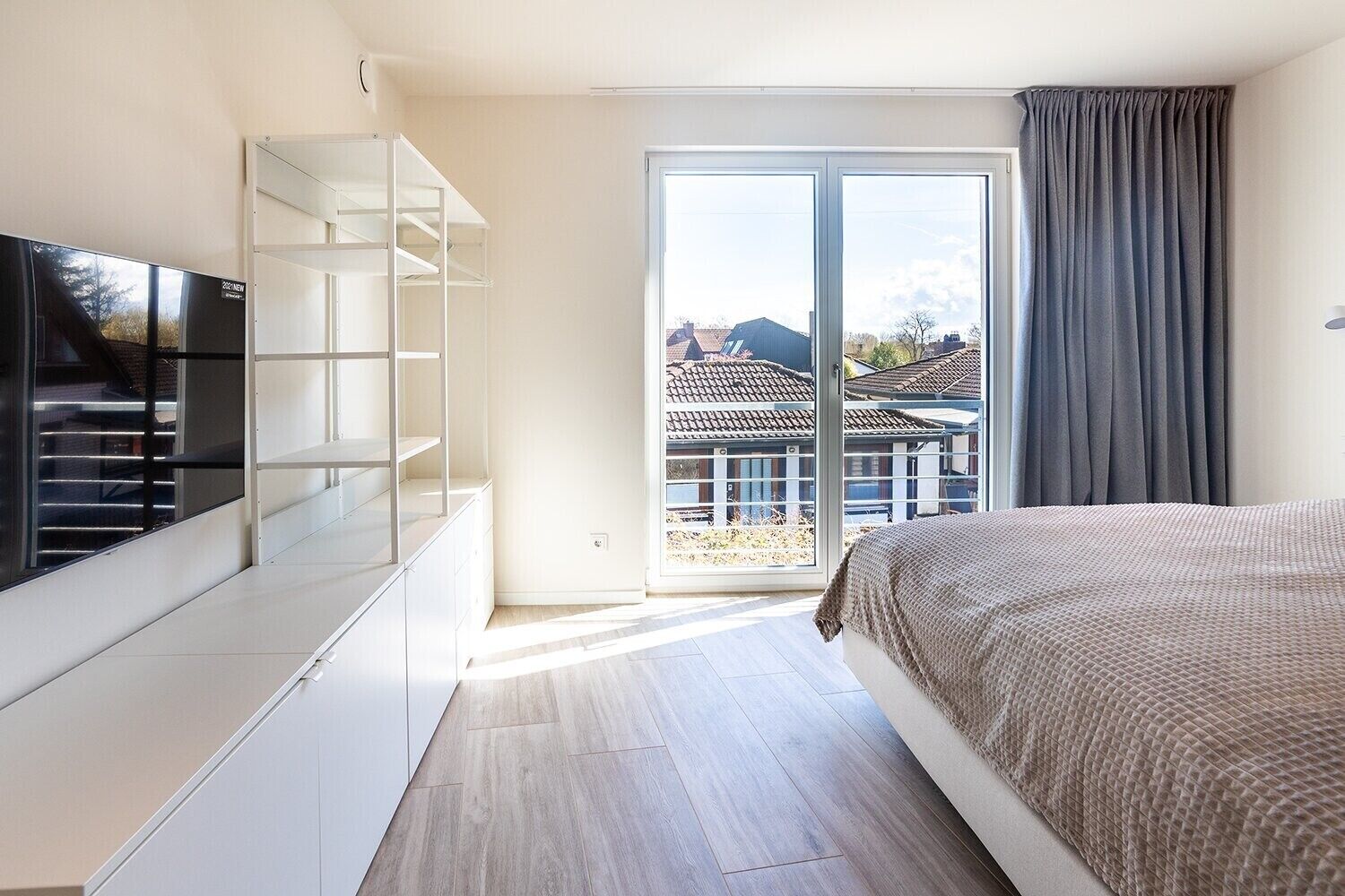 Et moderne soveværelse med seng, fjernsyn, garderobeskab og en skydedør til en balkon.