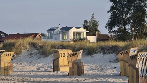 Hiekkarannalla on numeroilla 1289, 1333, 1388, 1355 ja 137 varustettuja rantatuoleja, ja taustalla näkyy talo.