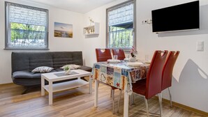 A modern living room with a sofa, dining table, chairs, and a flat-screen TV mounted on the wall.