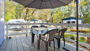 A covered outdoor area with a table and chairs, a large umbrella, and a view of cabins in the background.