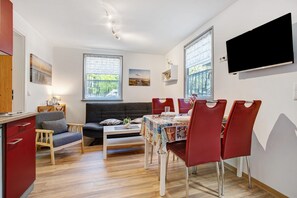 Un salon moderne avec une table à manger, des chaises rouges, un canapé et un téléviseur fixé au mur.