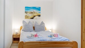 A neatly made bed with pillows, a bedside table with a lamp, and a painting of a landscape on the wall.