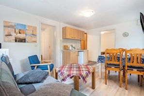 Un espacio habitable pequeño con una mesa de comedor, sillas, sofá y una zona de cocina, además de un reloj en la pared.