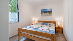 A bedroom with a wooden bed, a nightstand, a wall-mounted painting, and a window with curtains.