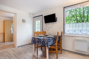 Un comedor con una mesa preparada para dos personas, un reloj en la pared y un televisor montado sobre la mesa.