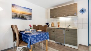 Zona pranzo con tavolo apparecchiato per due, cucina con pensili in legno e un orologio a parete.
