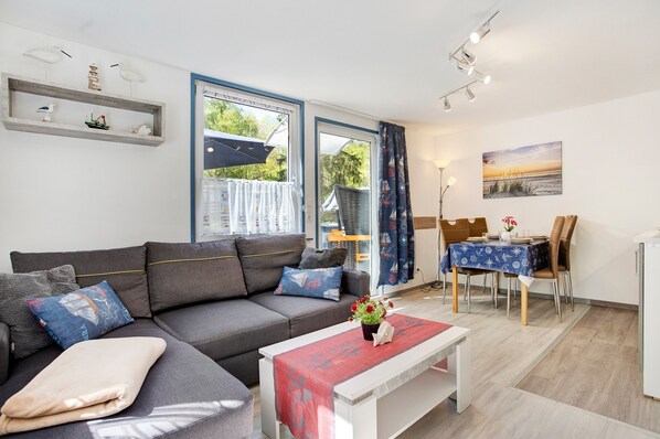 A modern living room with a sofa, a dining table, and a kitchen area.
